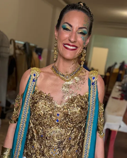 Festera sonriente con la mirada en turquesa y oro, labios granates y pan de oro sobre el pecho