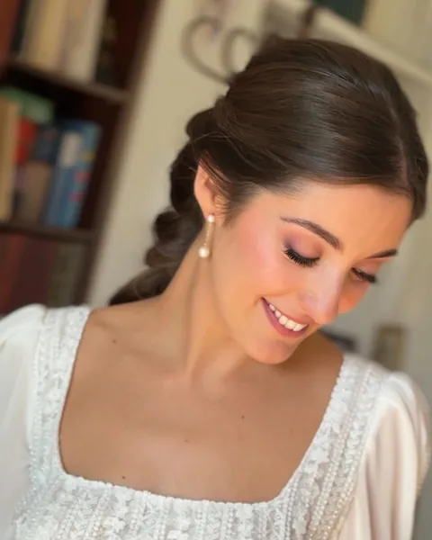 Novia con el pelo recogido en una trenza, mirando hacia abajo con una sonrisa