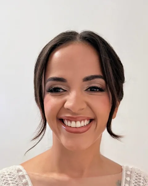 Novia con el pelo oscuro recogido y mechones sueltos, sonriendo a cámara